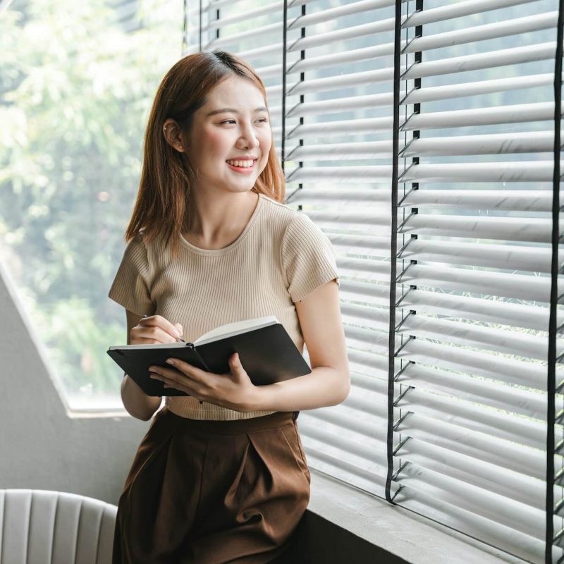 smiling-asian-woman-holding-a-note-in-hand-and-standing-near-window-startup-business-asian-woman-onl.jpg